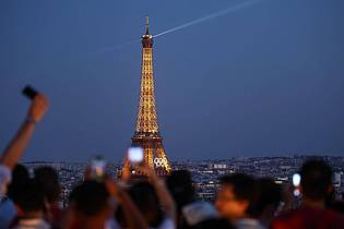 Jan Woitas/dpa | Paris im Sommer 2024 - besonders beliebt: Touristen fotografieren den Eiffelturm mit den Olympischen Ringen von der Terrasse des Triumphbogens. (Archivbild)