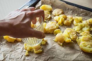 Christin Klose/dpa-tmn | Die gekochten Kartoffeln kommen auf ein Backblech und werden mit einem Glas zerdrückt. Mit Olivenöl bepinseln und Salzflocken bestreuen, dann 40 bis 45 Minuten knusprig backen.