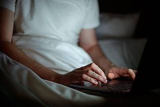 Sina Schuldt/dpa/dpa-tmn | Gemütlich im Bett zu arbeiten ist verlockend, doch Notebooks sollten auf festen und ebenen Unterlagen stehen, damit die Luftzirkulation nicht behindert wird.