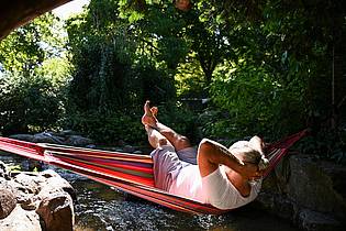 Katharina Kausche/dpa | Ein Mann schaukelt im Berliner in einer Hängematte über dem Wasser. 