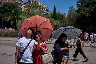 Emilio Morenatti/AP/dpa | Touristen schützen sich amvor der Kirche Sagrada Familia mit Regenschirmen vor der Sonne. 